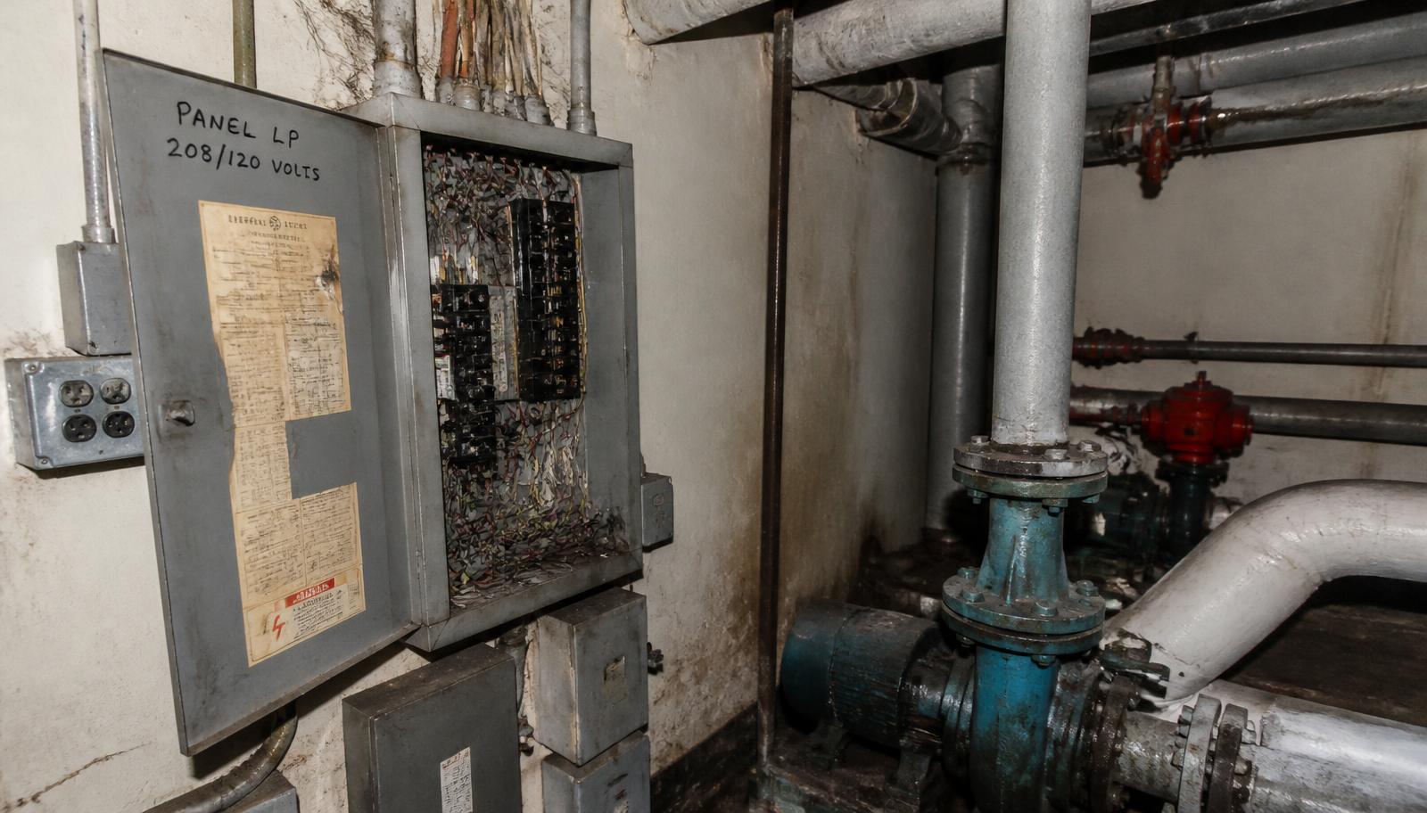 Casa de máquinas com quadro elétrico aberto, tubulações e bomba de água
